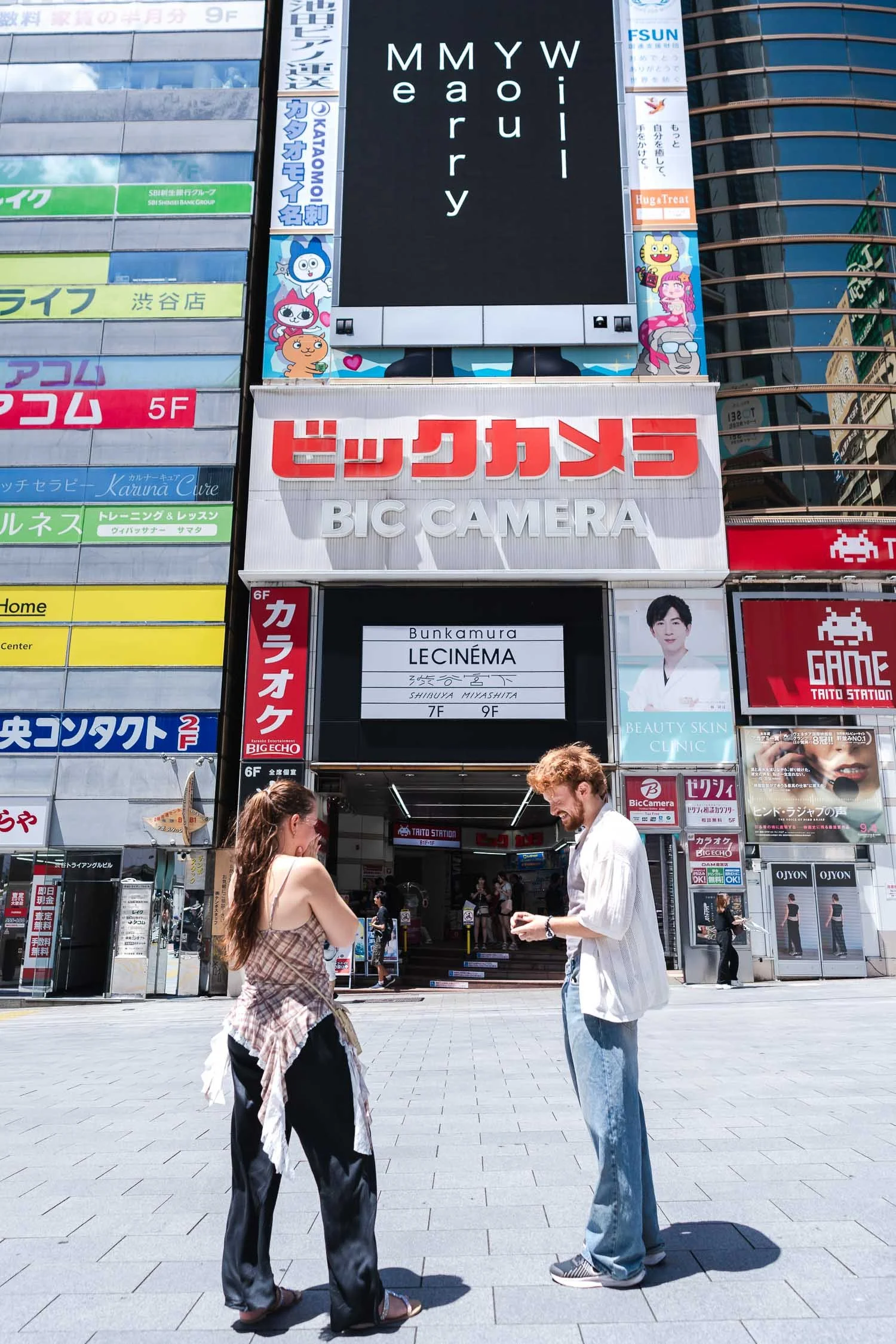Woman covering her face in shock during surprise proposal reaction below Shibuya digital billboard display