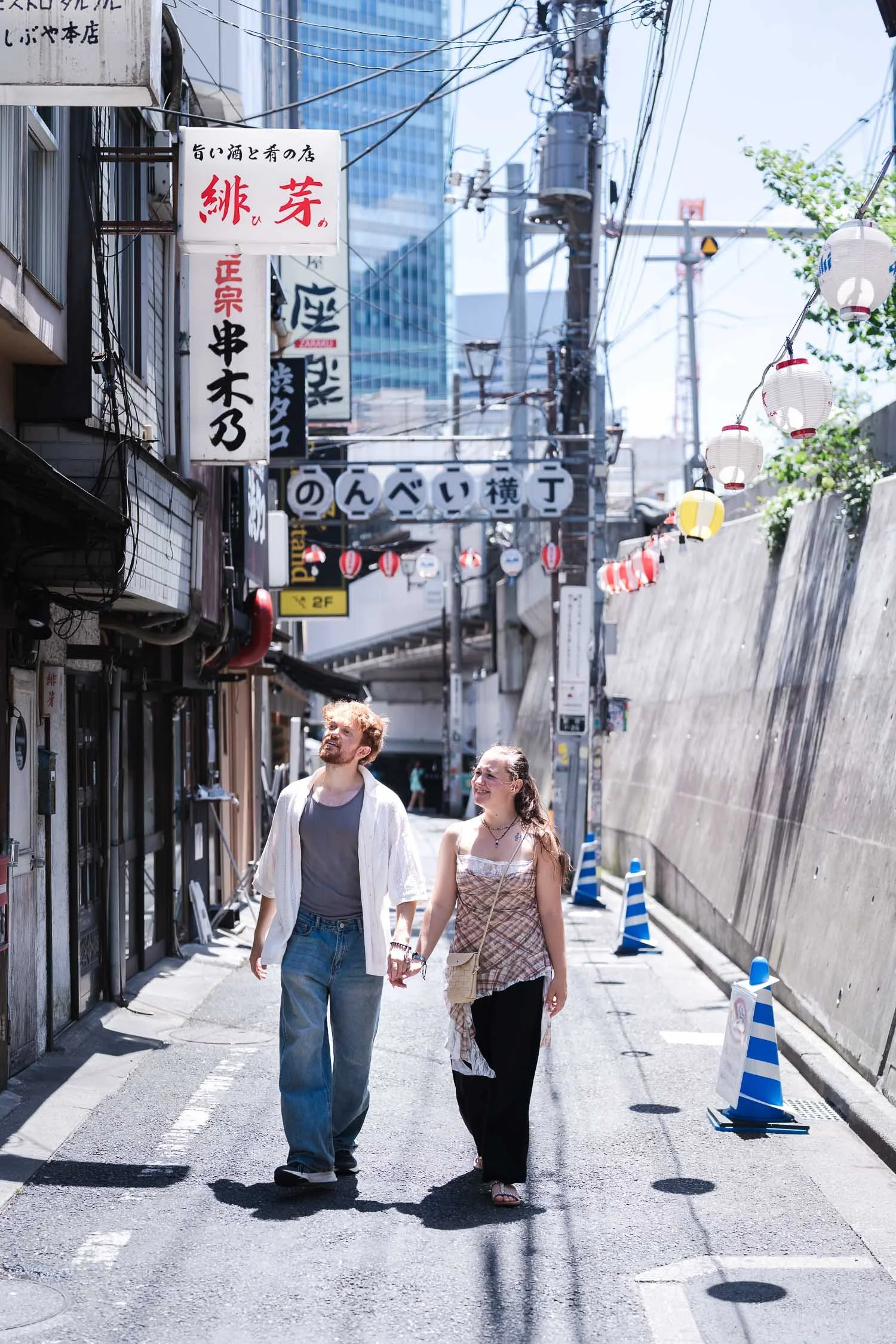 Couple walking hand in hand through Nonbei Yokocho lantern-lined alley in Shibuya Tokyo