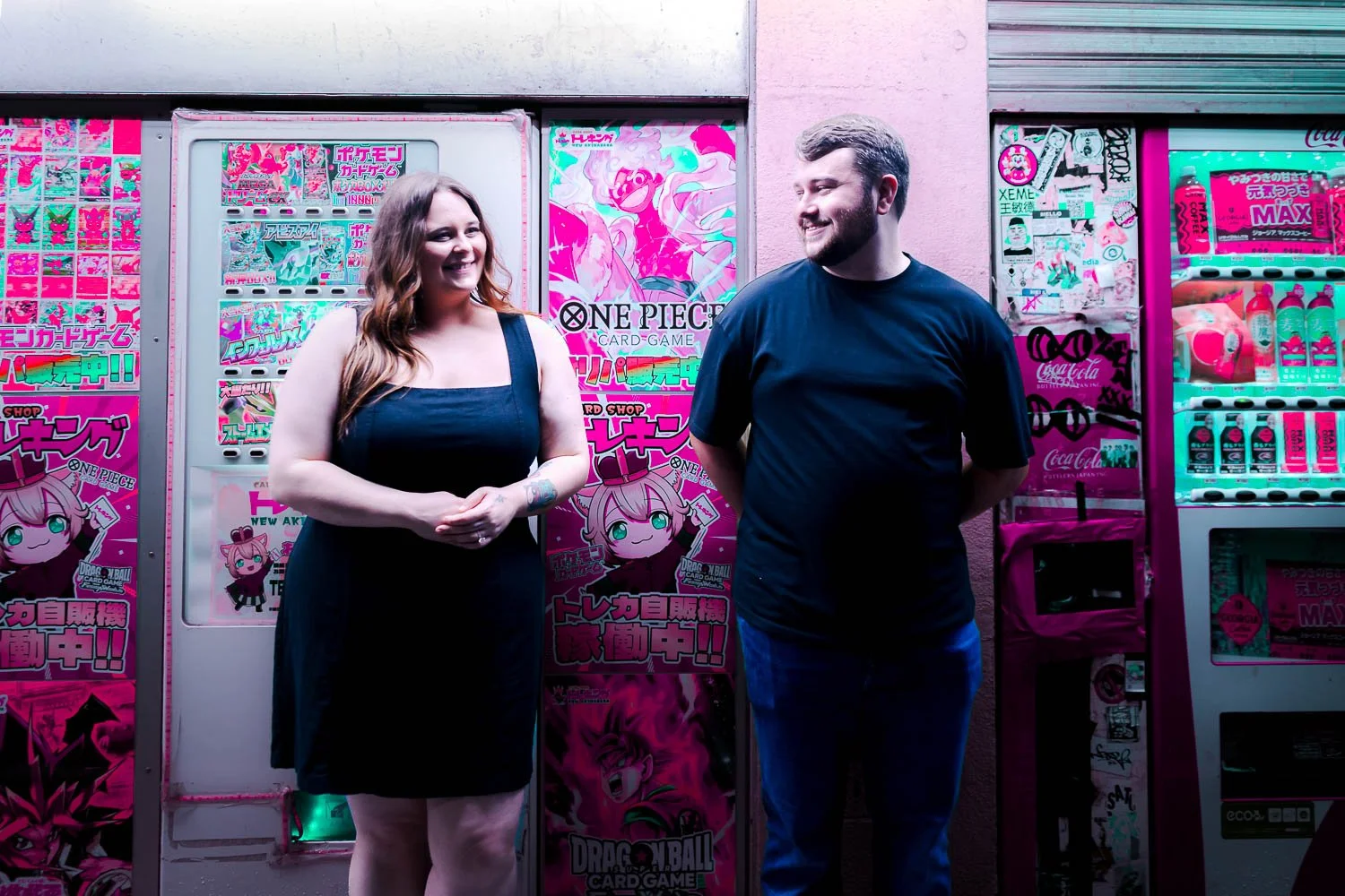 Couple smiling in front of a colorful Akihabara trading card shop covered in anime and Pokémon posters