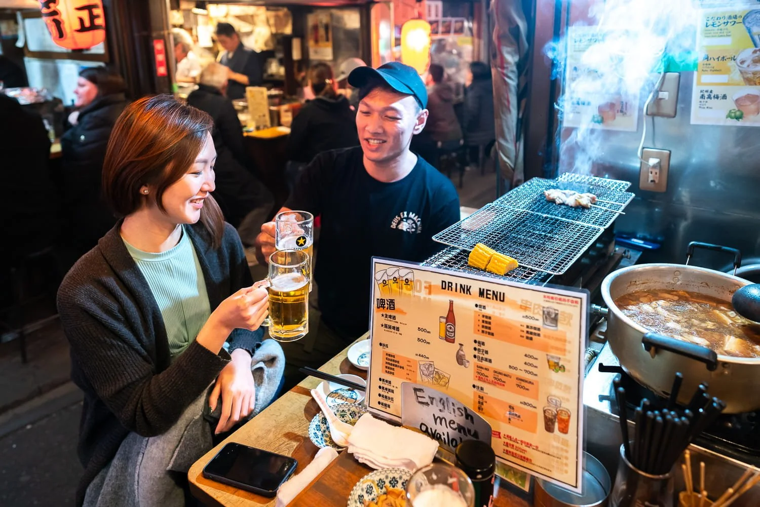 Local street food scene in Shinjuku Omoide Yokocho AKA Memory Lane where a couple enjoying street food (yakitori) & drinks.
