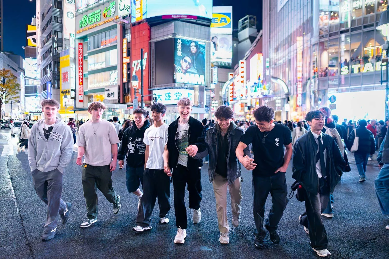 A group of male teenagers walking while laughing at Shibuya Scramble Crossing, Tokyo during an evening neon photoshoot