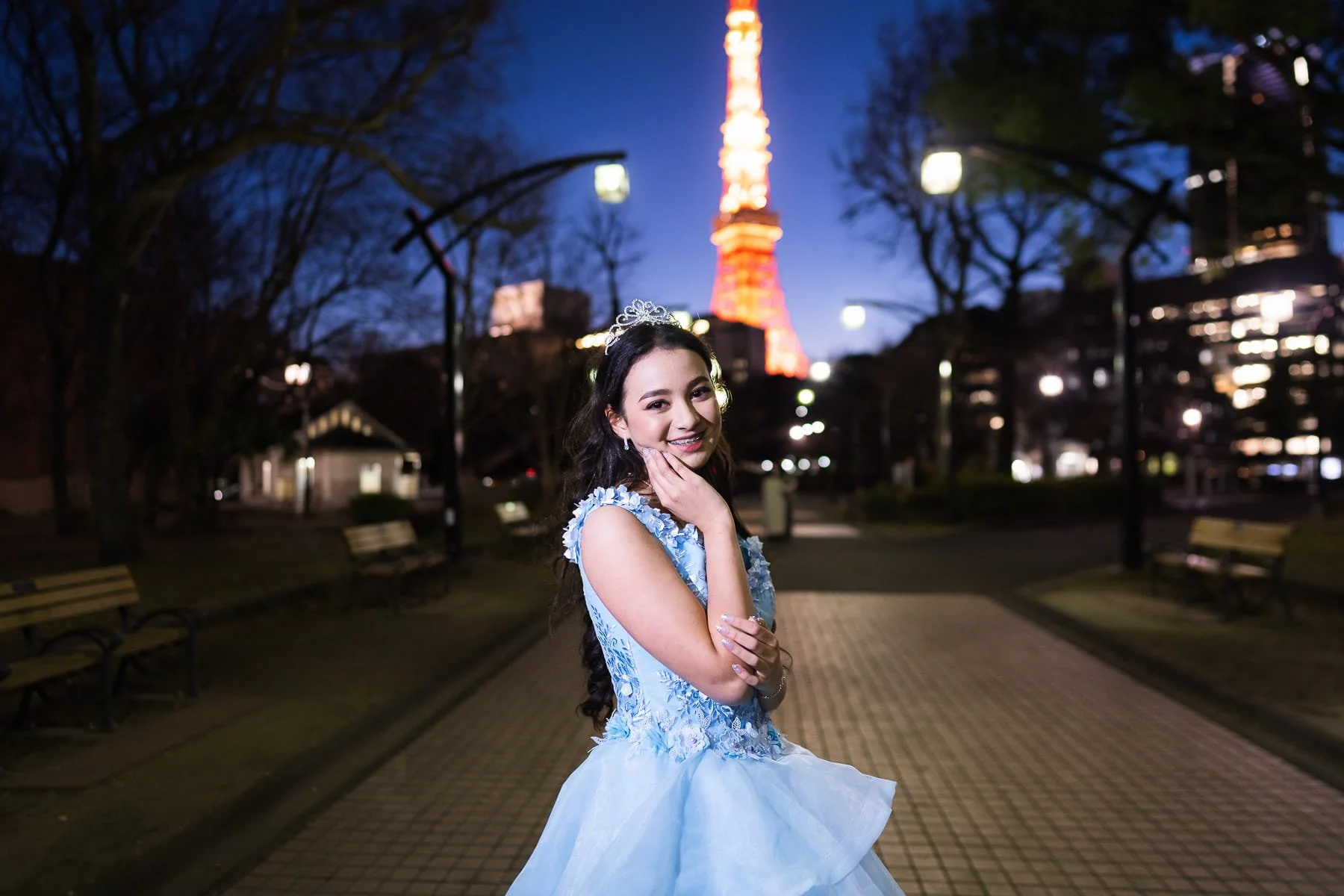 Quinceañera in a light blue gown and tiara posing at night with Tokyo Tower lit up in the background