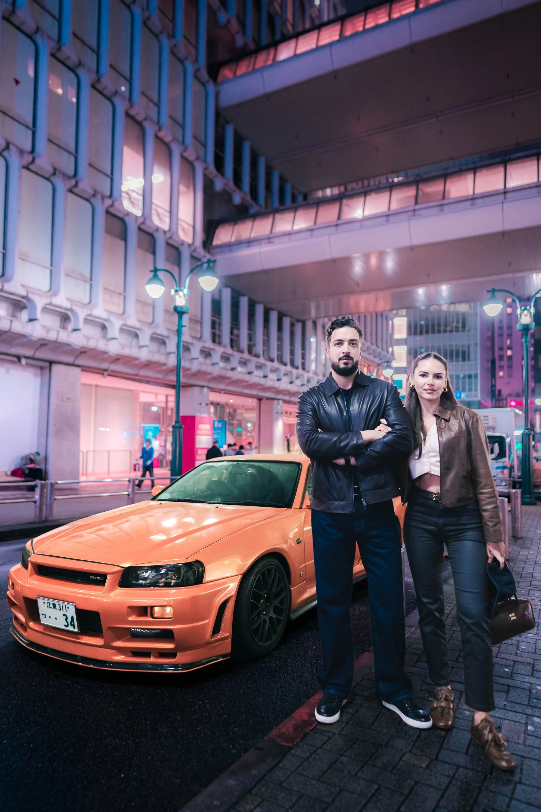 Tokyo cyberpunk photoshoot of a couple posing in front of orange Nissan Skyline, the scene resembles a poster of Fast & Furious, Tokyo Drift