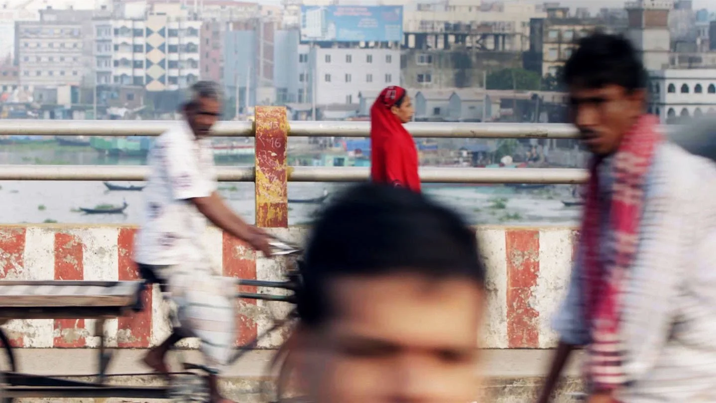 A view from a bridge in Dakkar Bangladesh. In the bvackground we see the skyline and in the foreground we see various users of the bridge - cyclists, and pedestrians in traditional Bengali attire