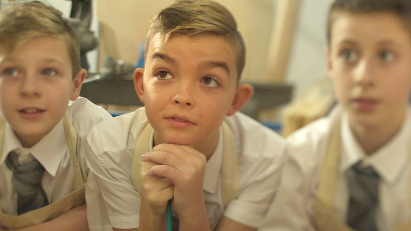 Three schoolboys in school uniform are paying attention to the teacher in a woodwork class