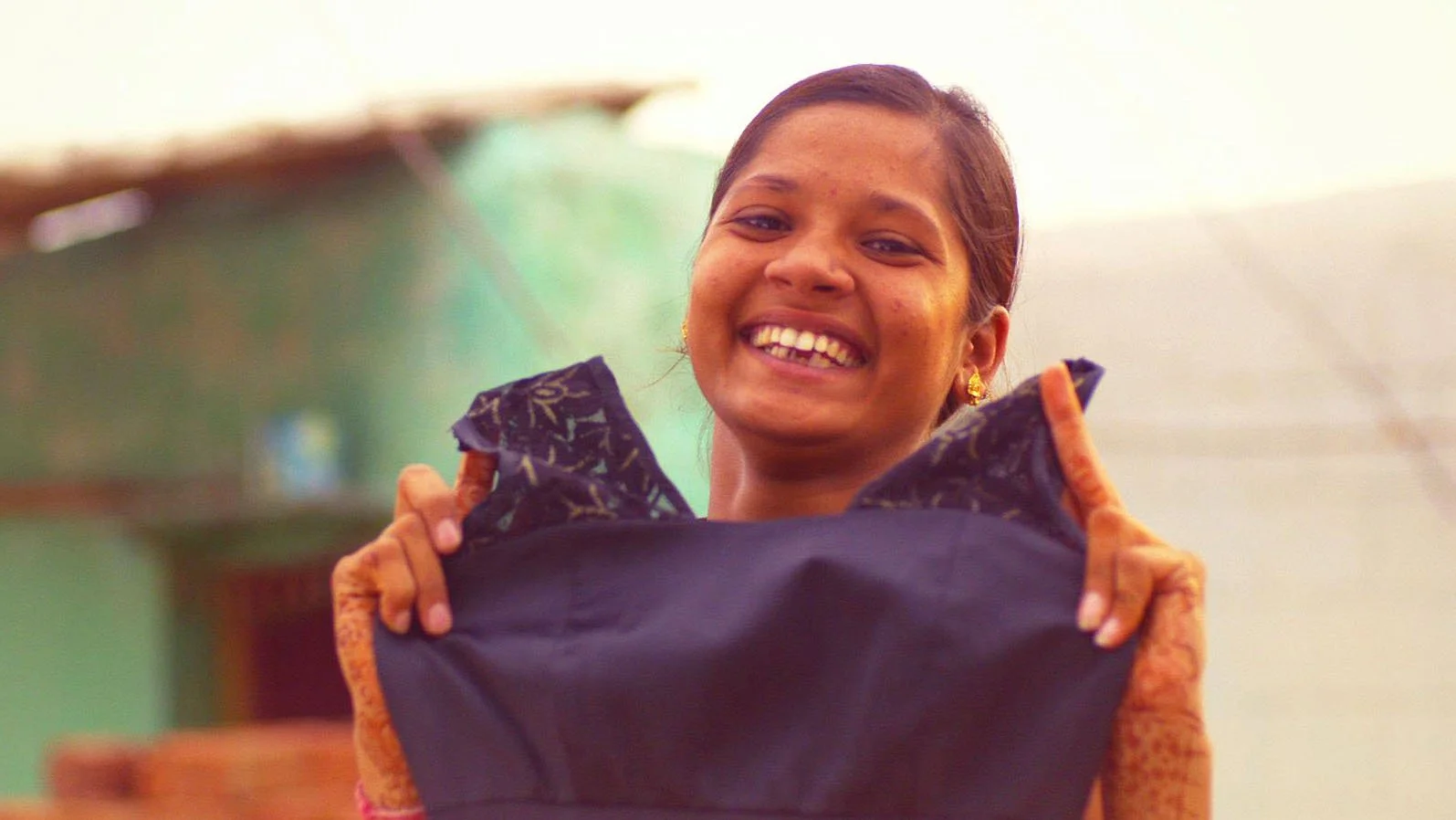 An Indian girl ina traditional village is excitedly holding up a black dress that she has designed