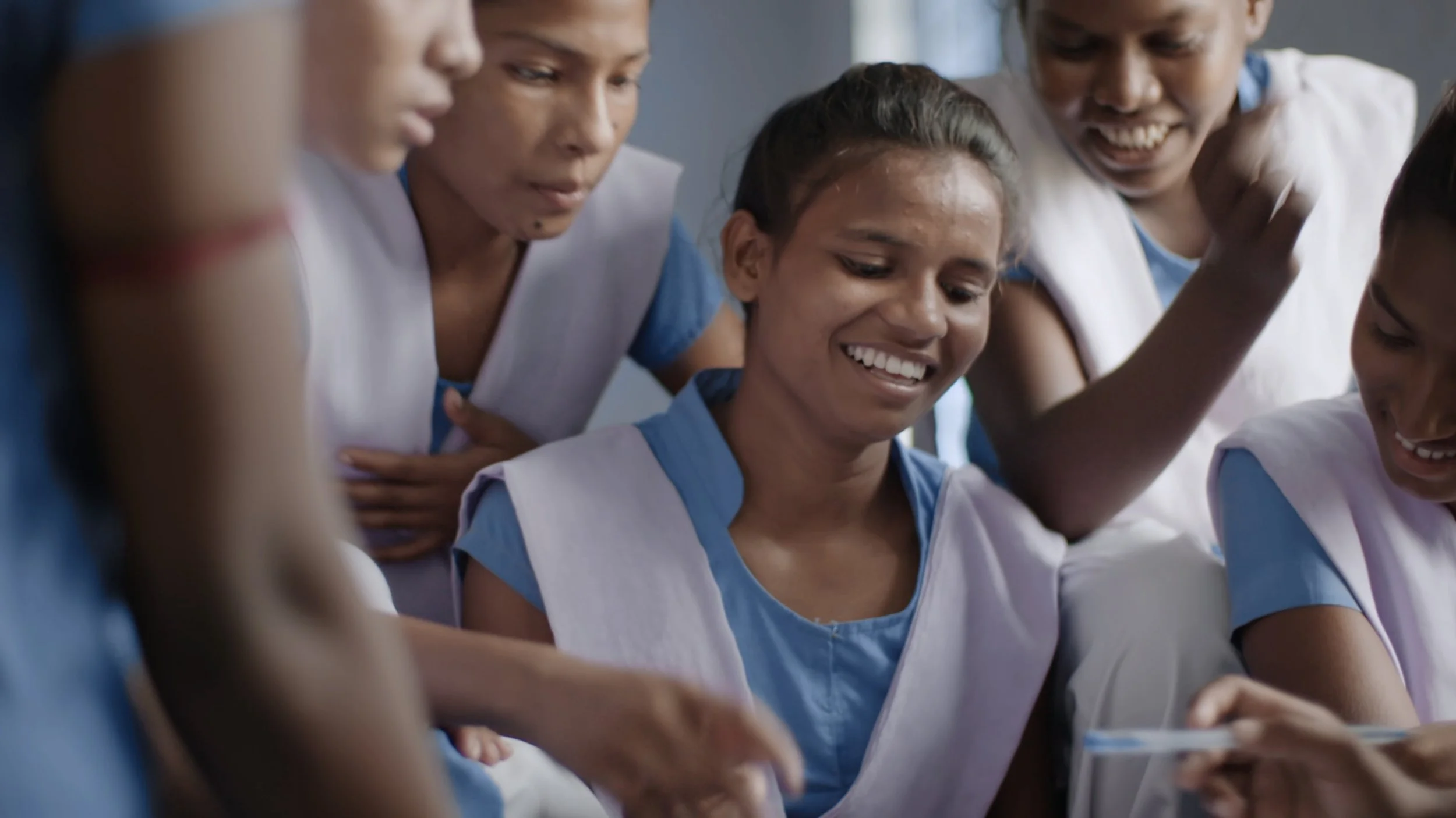 A group of Indian schoolchildren are having an animated discussion while seated on school desks in a classroom. They are wearing India style blue and white school uniforms