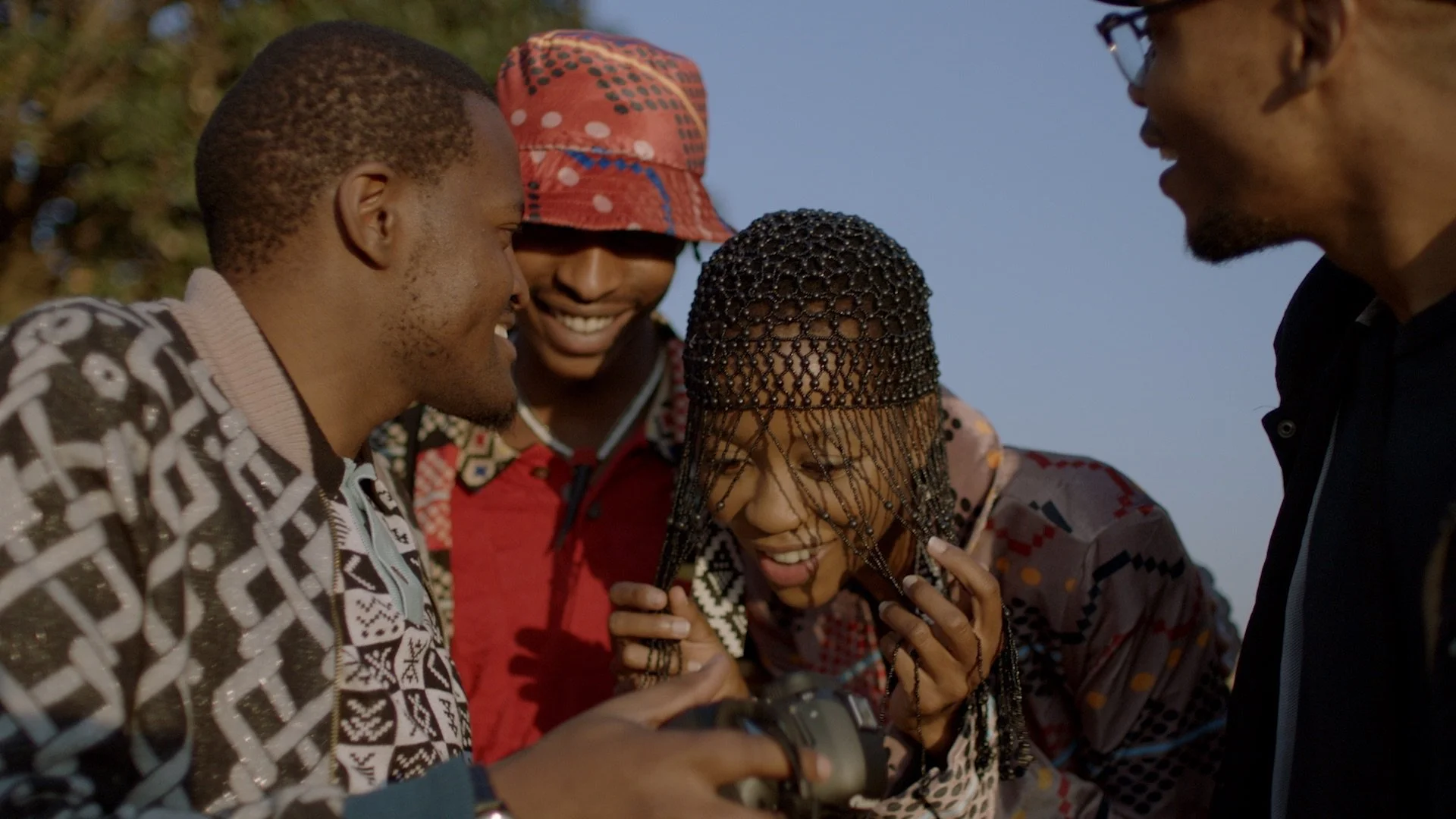 A group of young black South Africans in traditional Mxhosa designs are looking excitedly at the back of a photographers camera