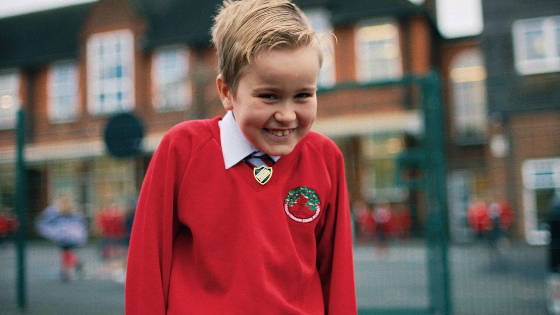A young boy in a red school uniform is playting and laughing in the playground of a Victorian school