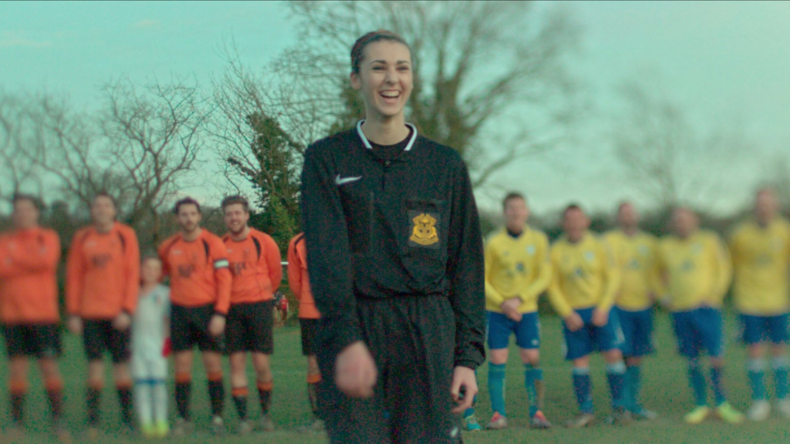 A teenaged girl is laughing as she poses for a photo with the two soccer teams she has just refereed a match for