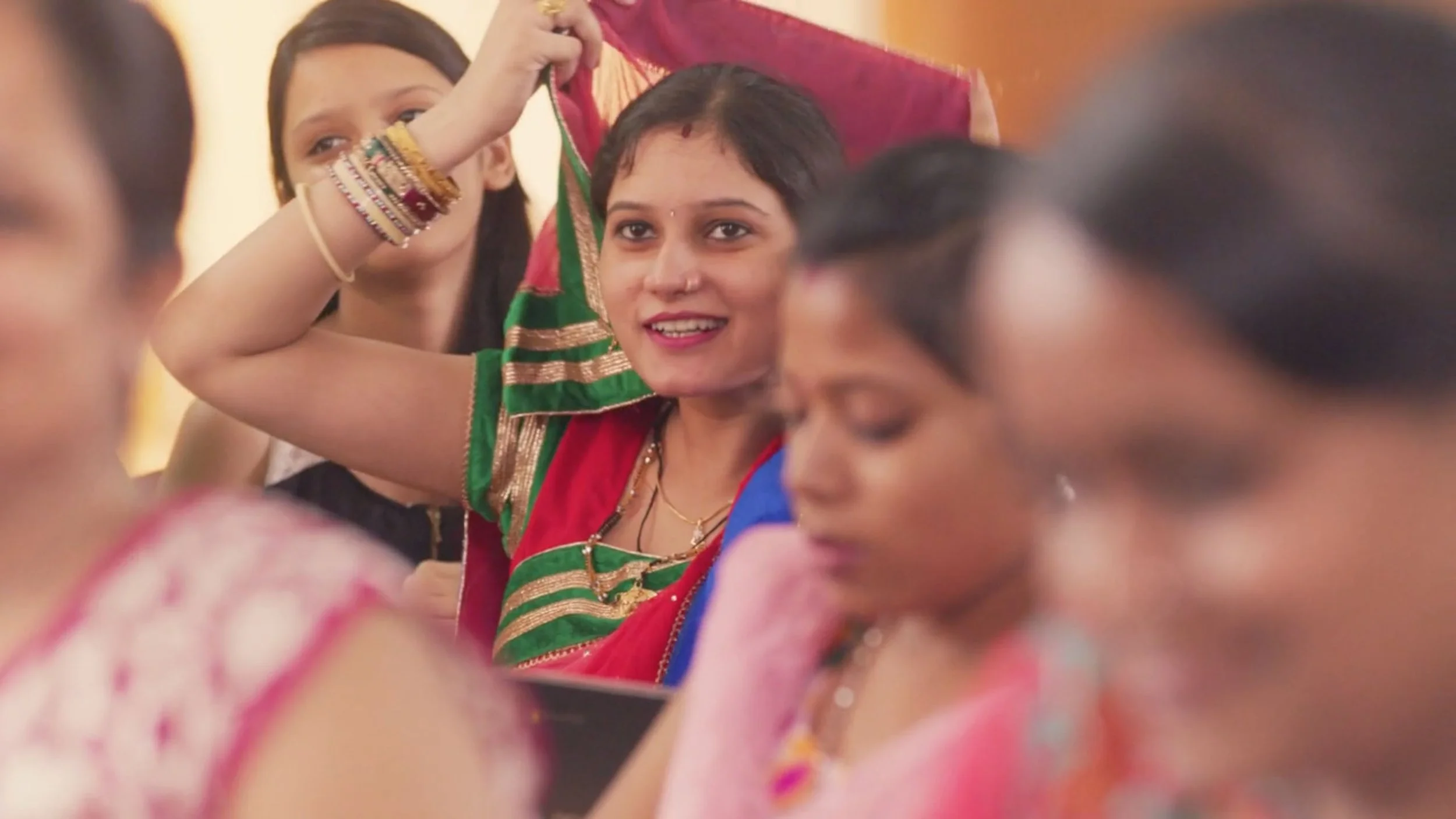 A group of Indian women. in a classroom are looking happily towards the front of the class. The womn in. the middle is adjusting her sari over her head