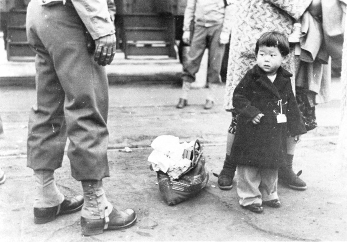A JAPANESE AMERICAN CHILD is tagged for incarcEration in Los Angeles, California. FrOM THE VISUAL COMMUNICATIONS ARCHIVES.