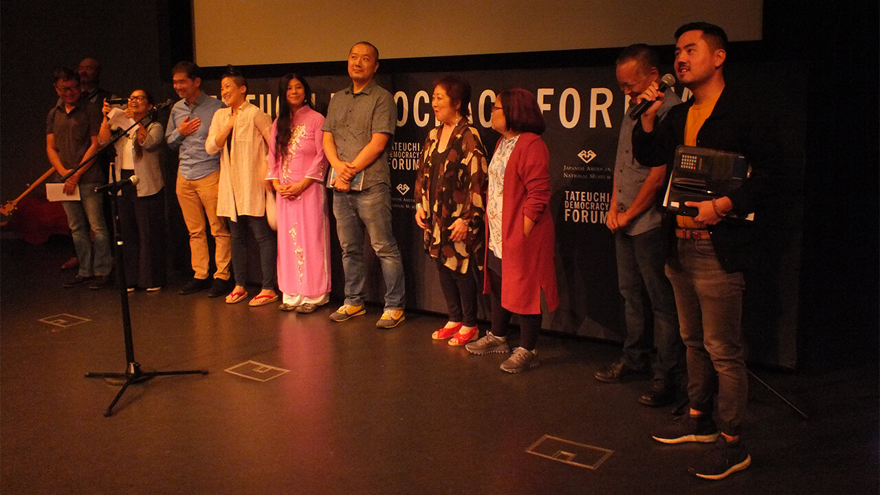 Host Sean Miura (far right): congratulates the artists whose works informed the “At First Light” program “Reflections/Refractions: 10 Works Inspired by “At First Light” at the Tateuchi Democracy Forum (from left): Eric C. Wat, Dom Magwili, Irene Suico Soriano, Stan Yogi, Traci Kato-Kiriyama, Teresa Mei Chuc, Kenji Liu, Miya Iwataki, Naomi Hirahara, and Taiji Miyagawa. (Photo: Florante Ibanez/Visual Communications Photographic Archive)
