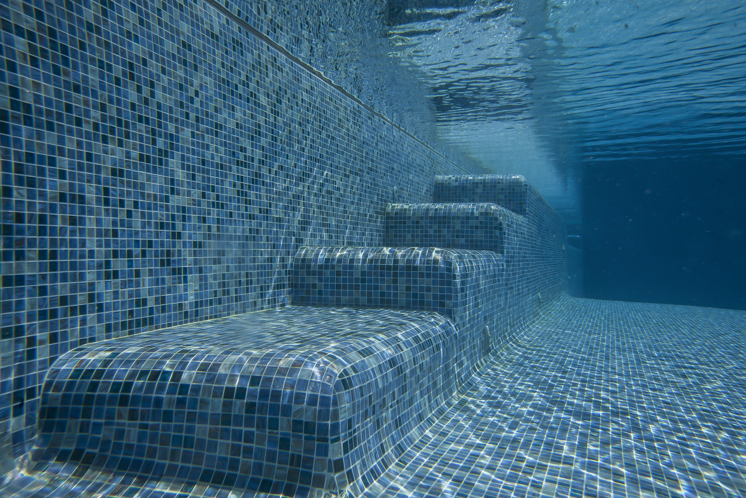 The custom blend Italian glass tile was installed in smooth radius curves over shelves, benches, and steps for swimmer comfort.