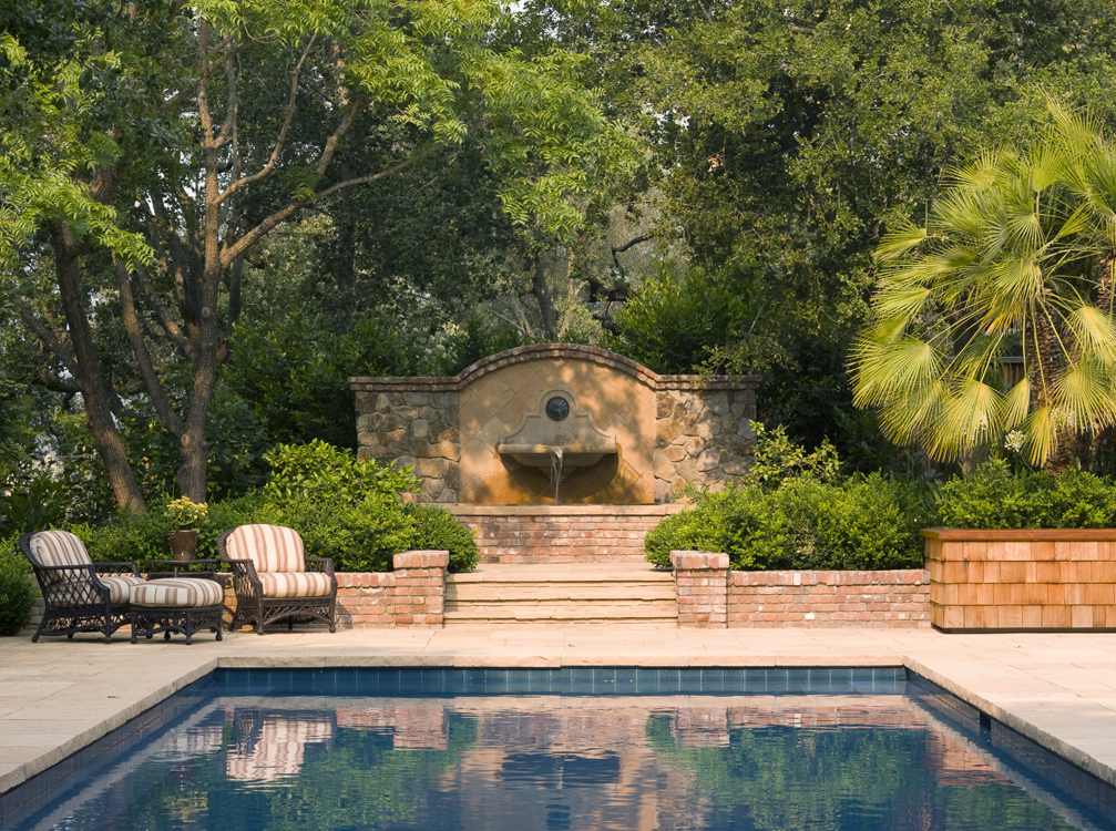 The original pool in this hilltop garden was not square and had to be replaced to add a safety cover, so the terraces were replaced as well with a light colored flagstone to collect the light when viewed from above. Garden walls were made of shingle
