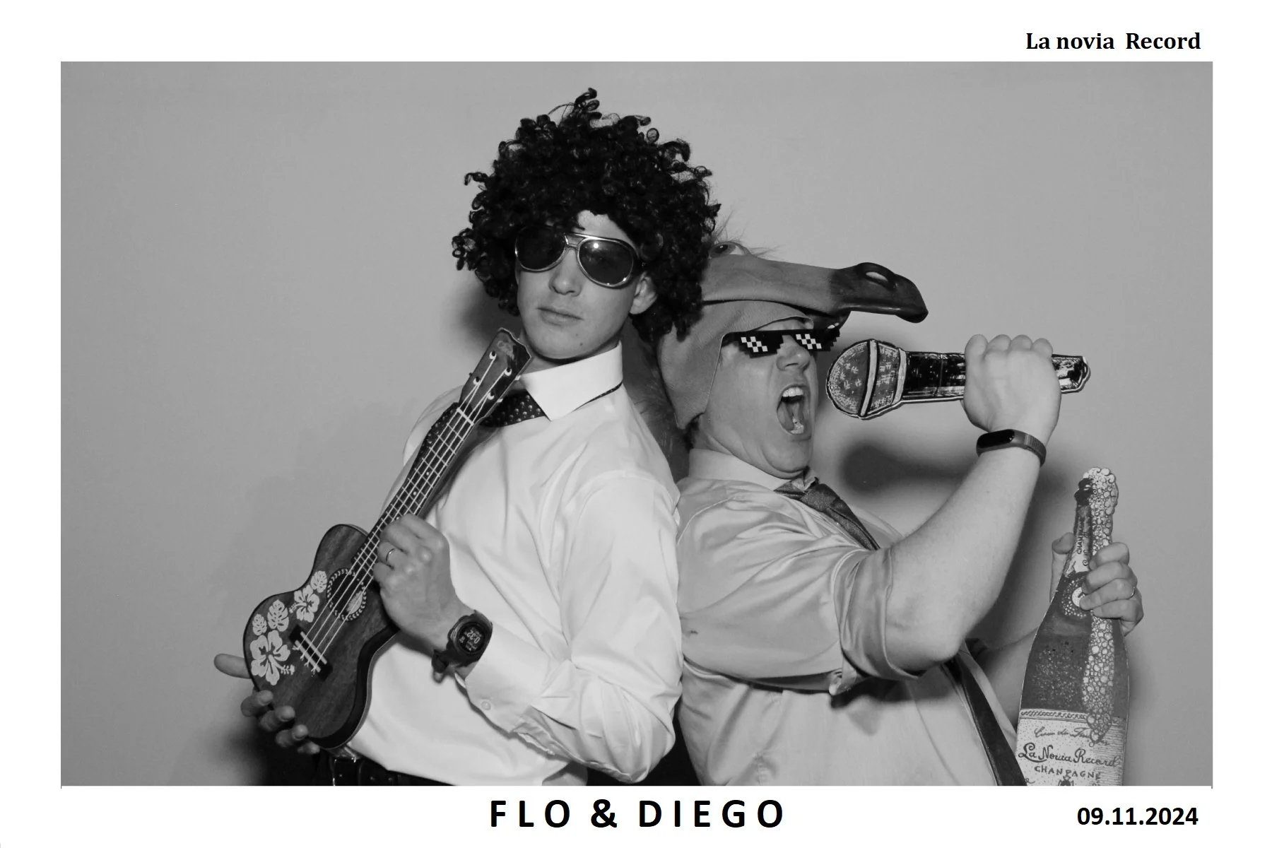 Dos personas en disfraces divertidos, uno con peluca afro, gafas oscuras y una guitarra pequeña decorada con flores, el otro con un sombrero, gafas de cuadrícula y un playboy, sosteniendo una botella de champagne y un micrófono, en una pose animada p