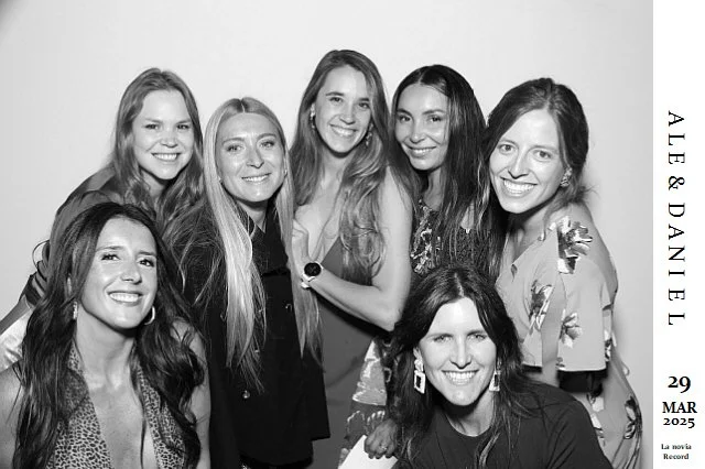 Grupo de siete mujeres sonriendo y posando juntas en una foto en blanco y negro, con texto en la esquina derecha que dice: 'Aler & Daniel, 29 MAR 2025, La novia recrea'.