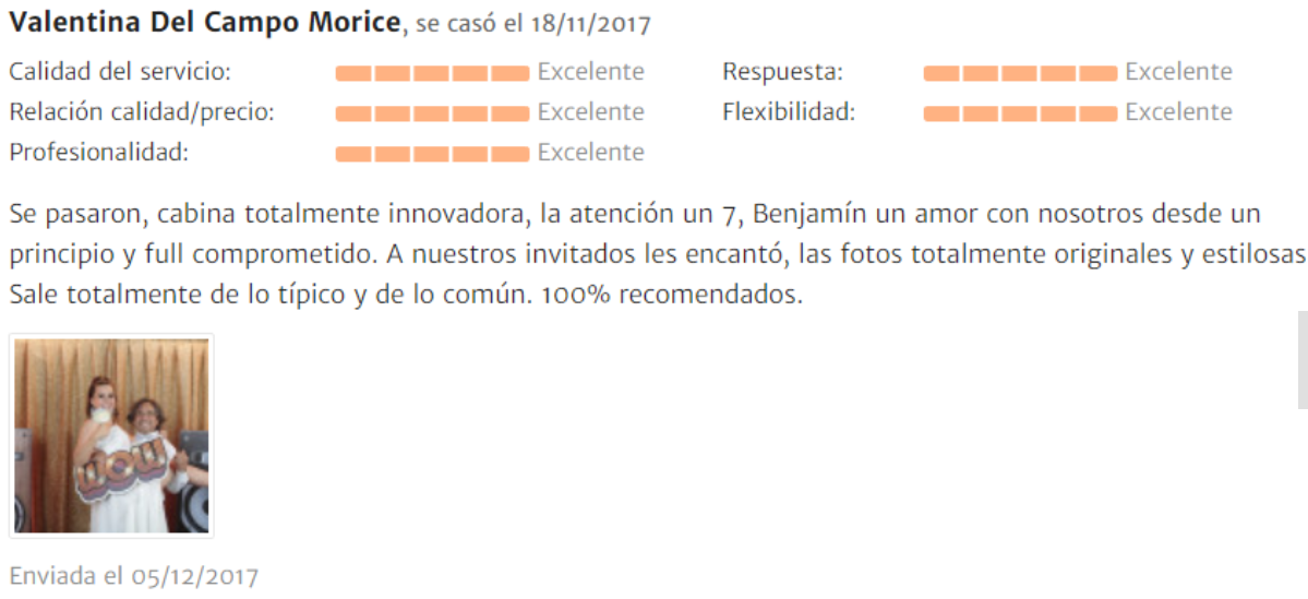 Una foto de dos mujeres en una fiesta, una de ellas con una máscara y ambas sosteniendo un cartel que dice "LOVE", en un ambiente con cortinas doradas.