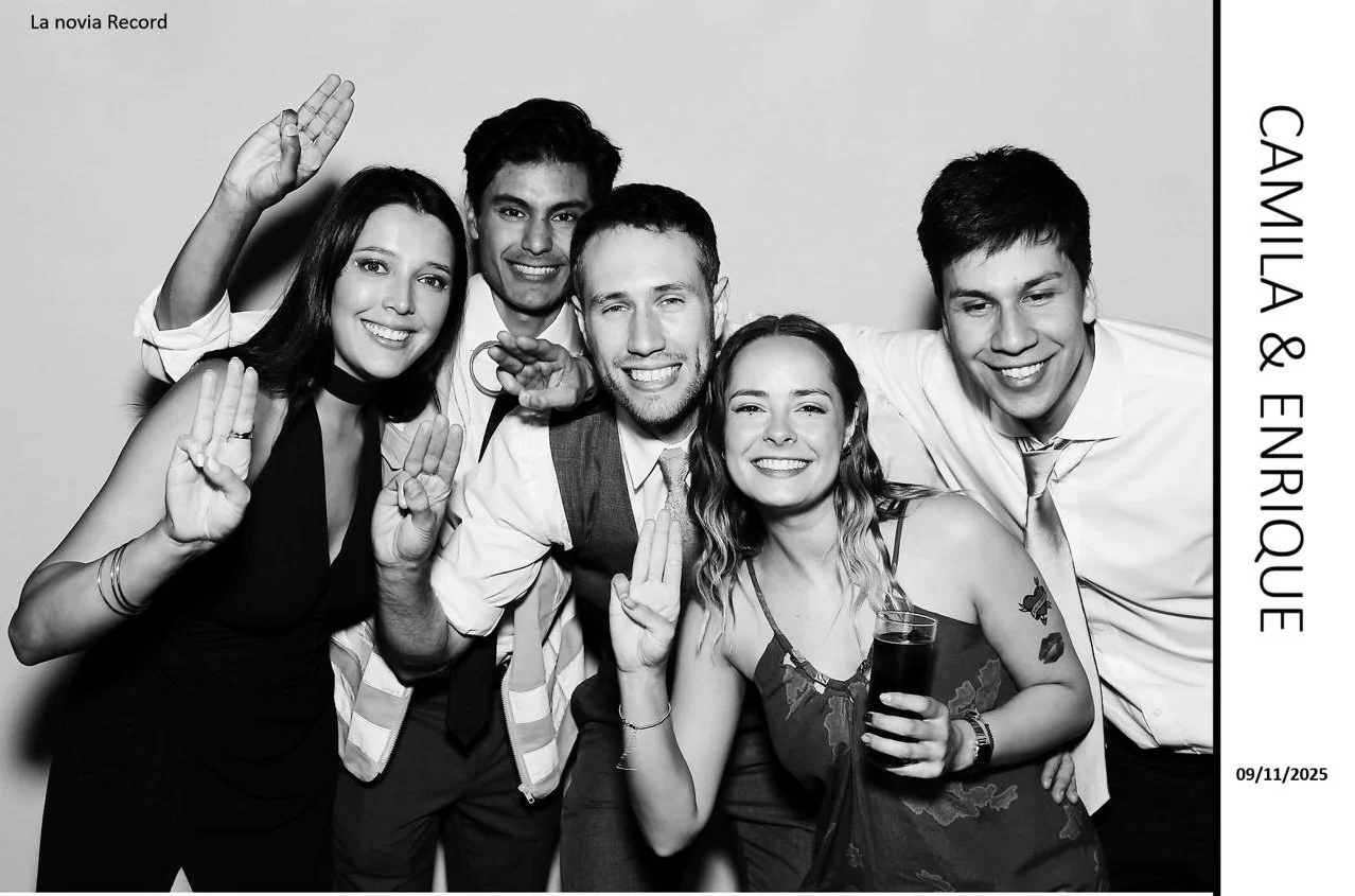 Grupo de seis personas sonriendo y saludando en una fotografía en blanco y negro, en una celebración de despedida de soltera, posando juntas con manos levantadas en señal de saludo y alegría, una mujer en el centro sostiene un vaso con bebida, todos 