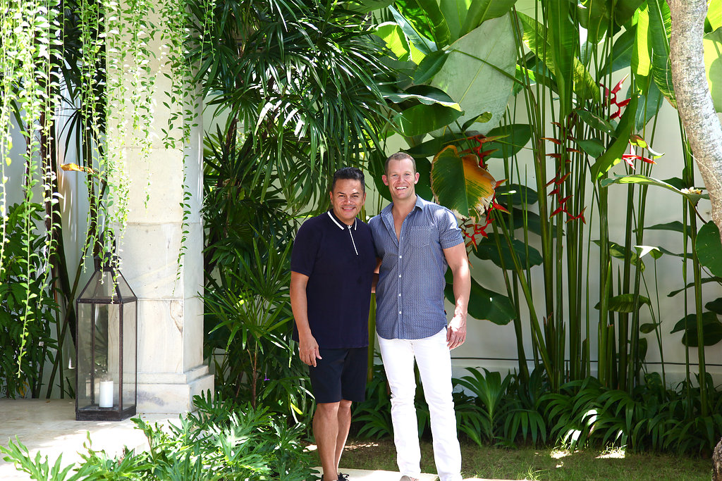 Two men standing side by side in a lush leafy area of their villa in Bali