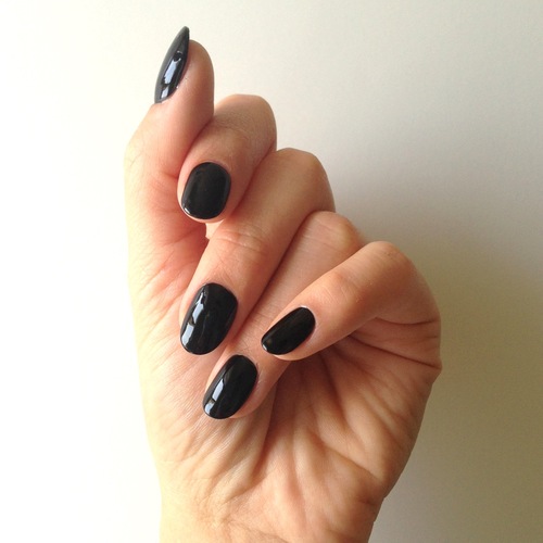 hand with black nails held up against a white wall