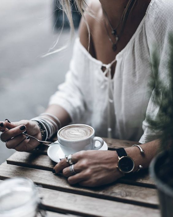 Woman in white off shoulder top and black watch holding spoon next to coffee 