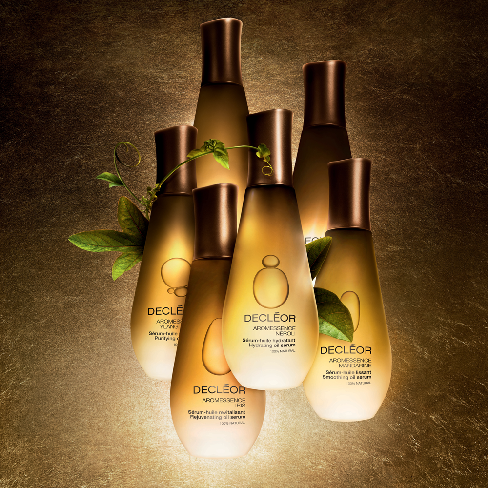 A group od Decleor beauty products arranged against a grainy brown background in gold bottles and leaves emerging from between them