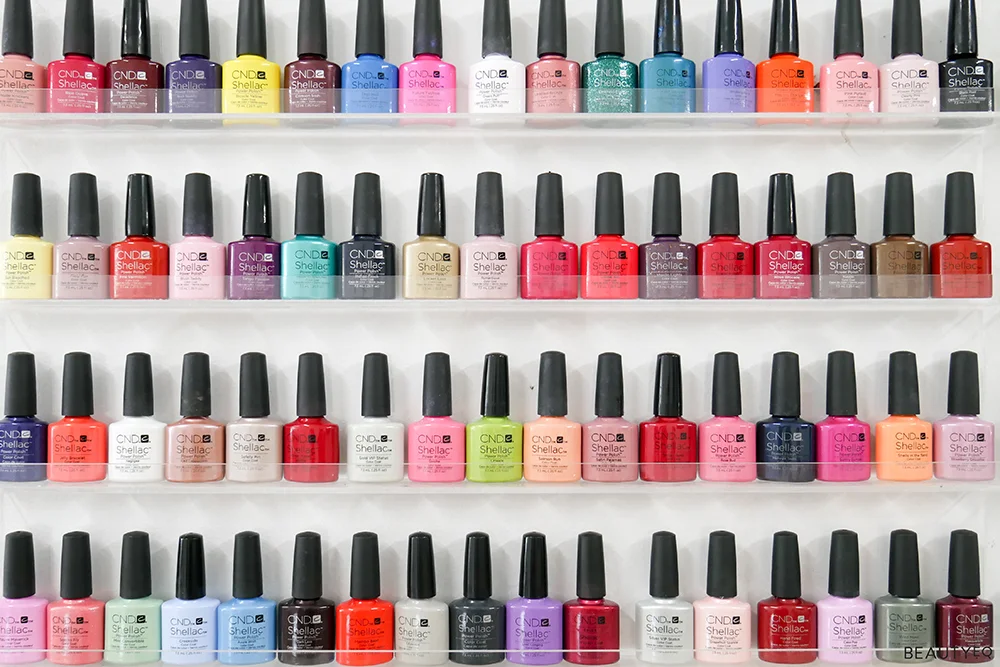 A wide range of nail polish lined up on shelves against a white wall