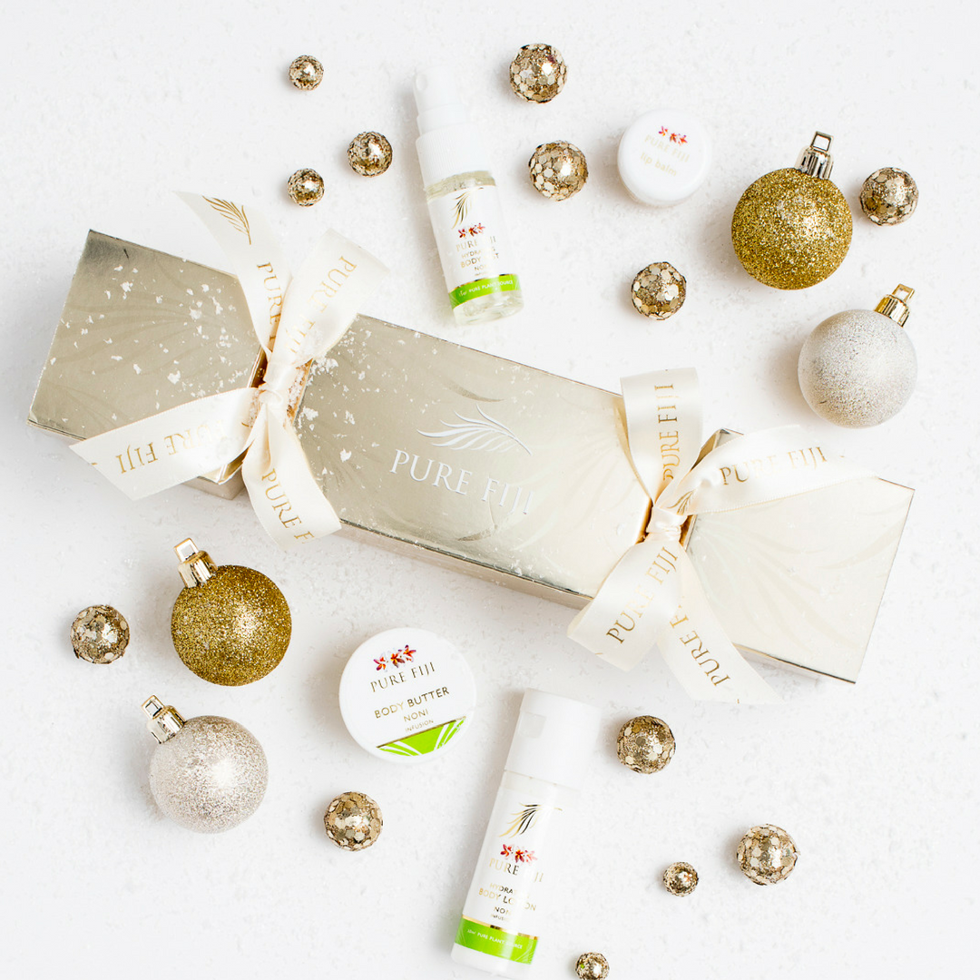 A range of Pure Fiji products arranged on a white table with a Christmas cracker in the middle and gold ornaments around them