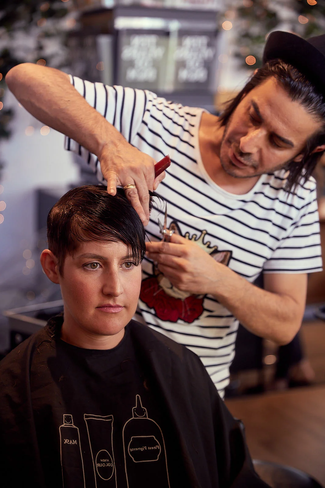 Brunette having hair cut by male hairdresser in stripe t-shirt