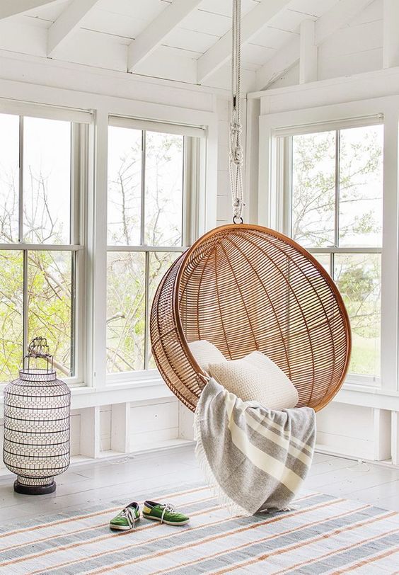 Light room with white walls and large windows with a swinging cane dome chair hanging 