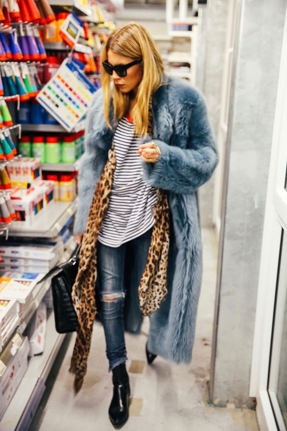 Model in a store wearing blue fur coat, leopard print scarf, striped top, blue ripped jeans and black boots