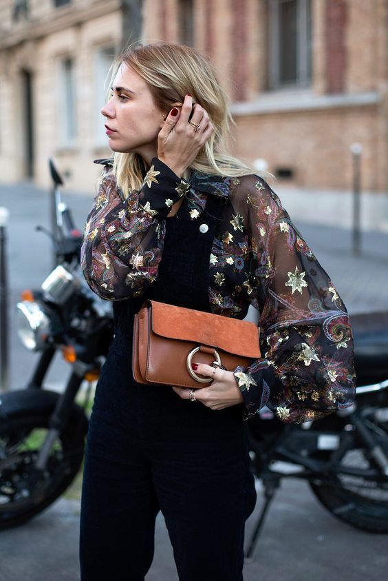 Blonde hair model wearing star print top black pants and holding leather clutch