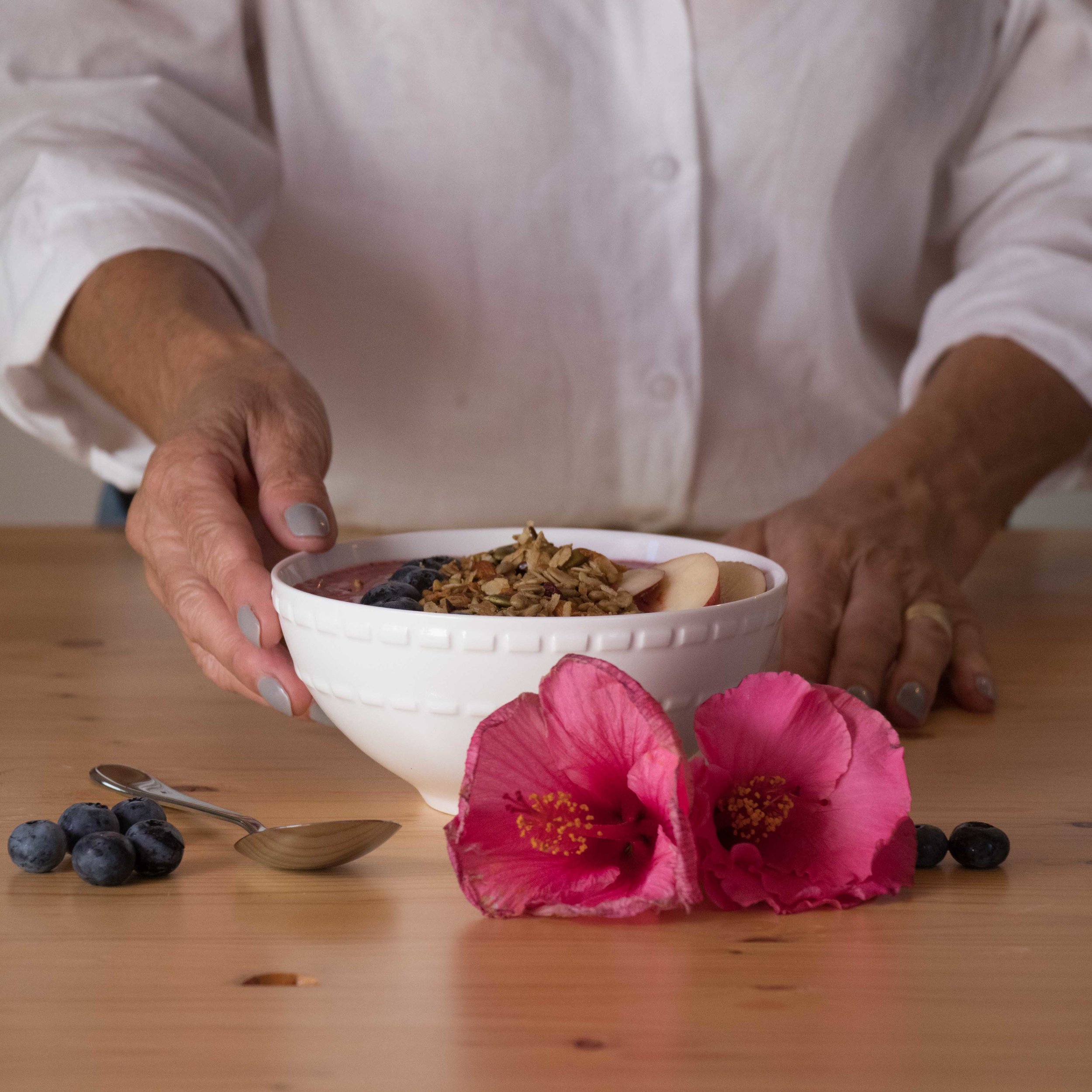 Smoothie bowl on wooden table next to pink flowers