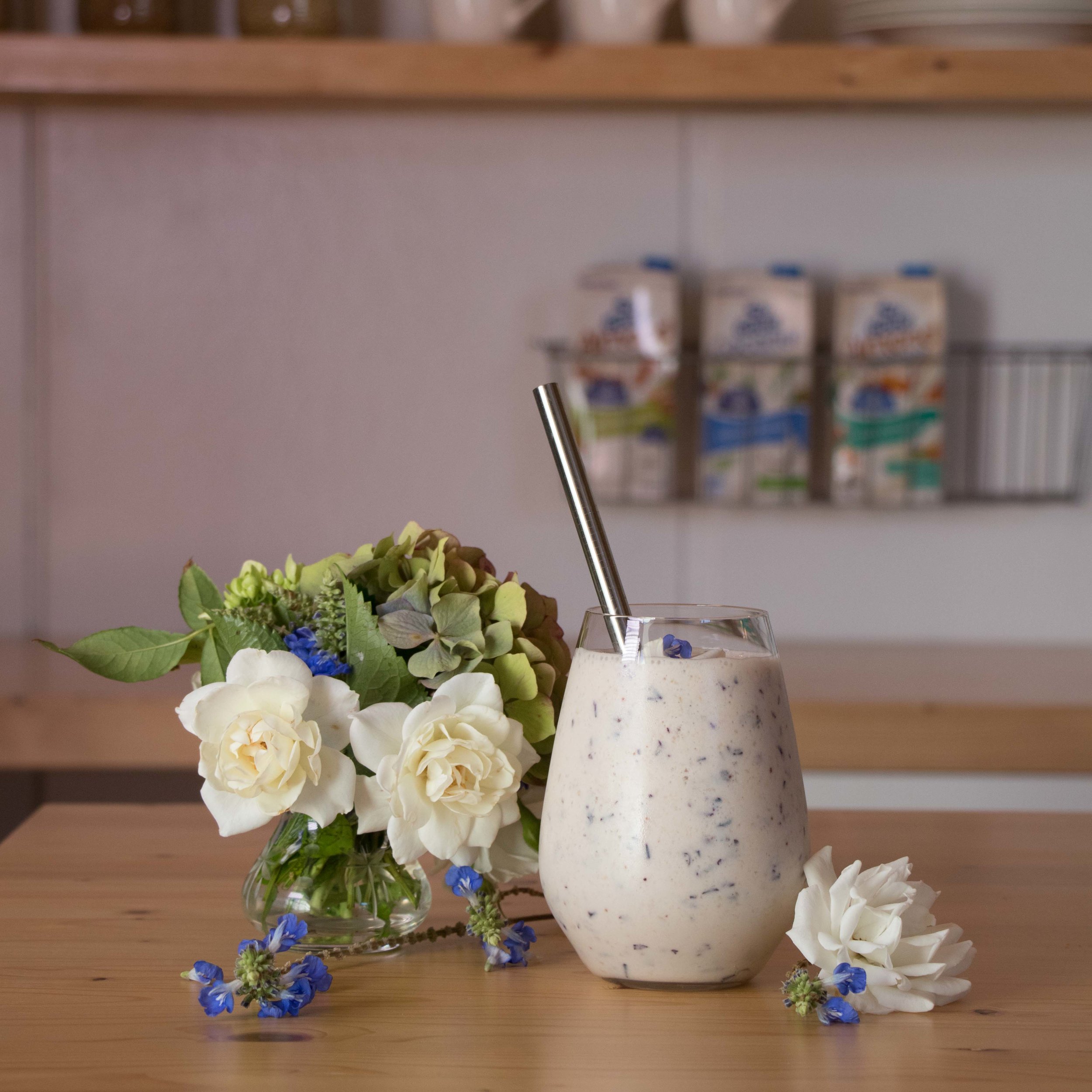 White smoothie on wooden table surrounded by flowers 