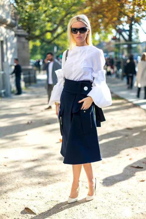 blonde model wearing white frilled long sleeve shirt with black skirt and black bag