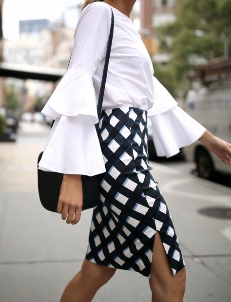 side profile of model wearing white frilled shirt with check skirt and black bag