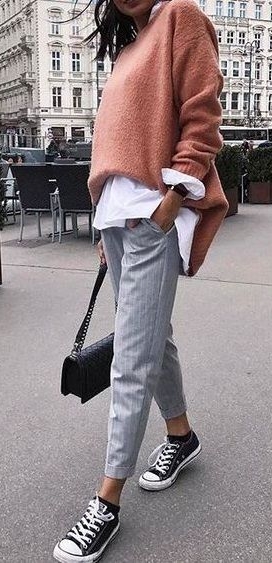Model wearing salmon sweater over white shirt and light blue jeans with chuck taylor shoes
