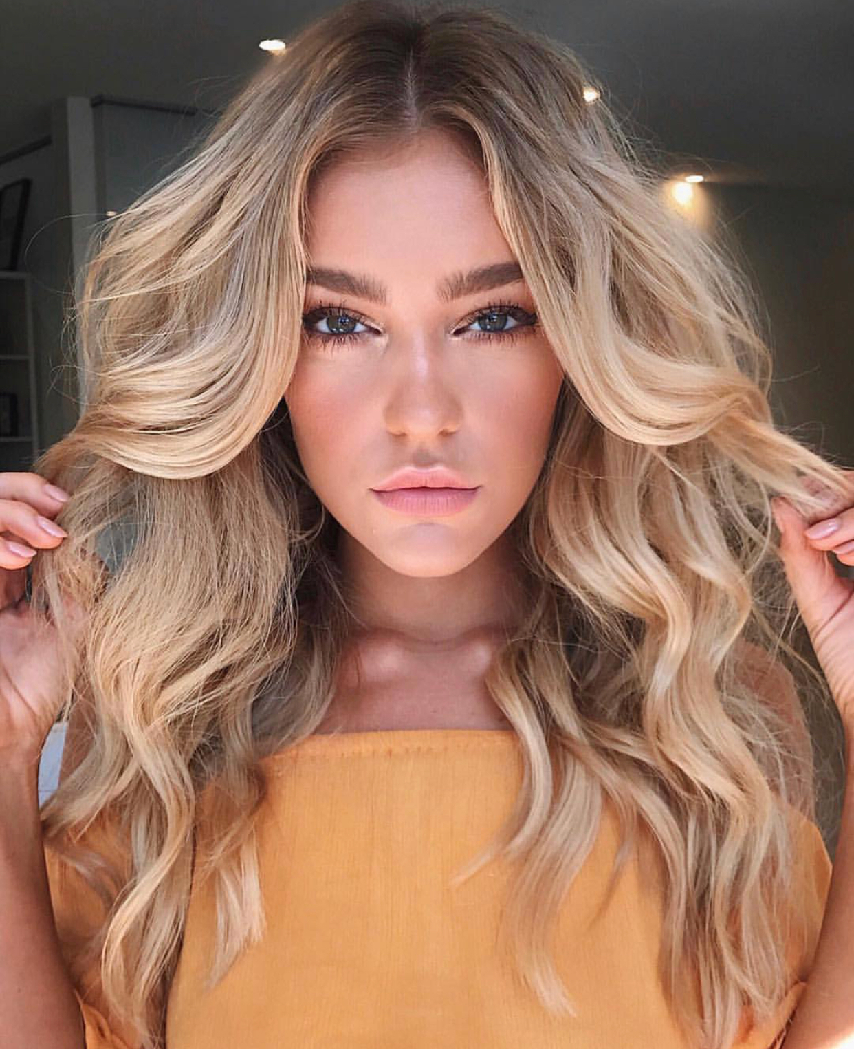 Blonde female model wearing yellow top holding her locks on each side