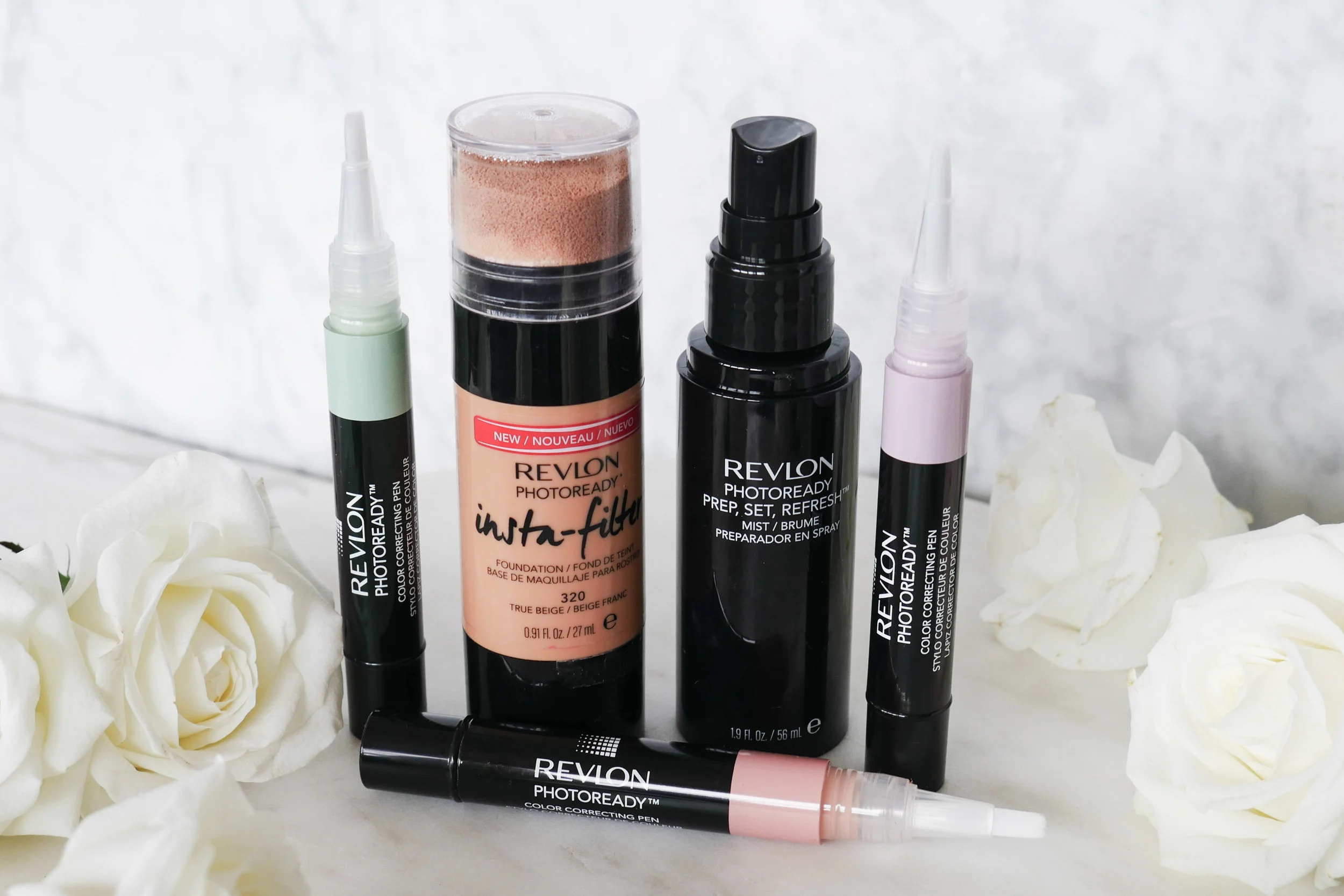 A range of Revlon beauty products arranged against a white marble background next to white flowers