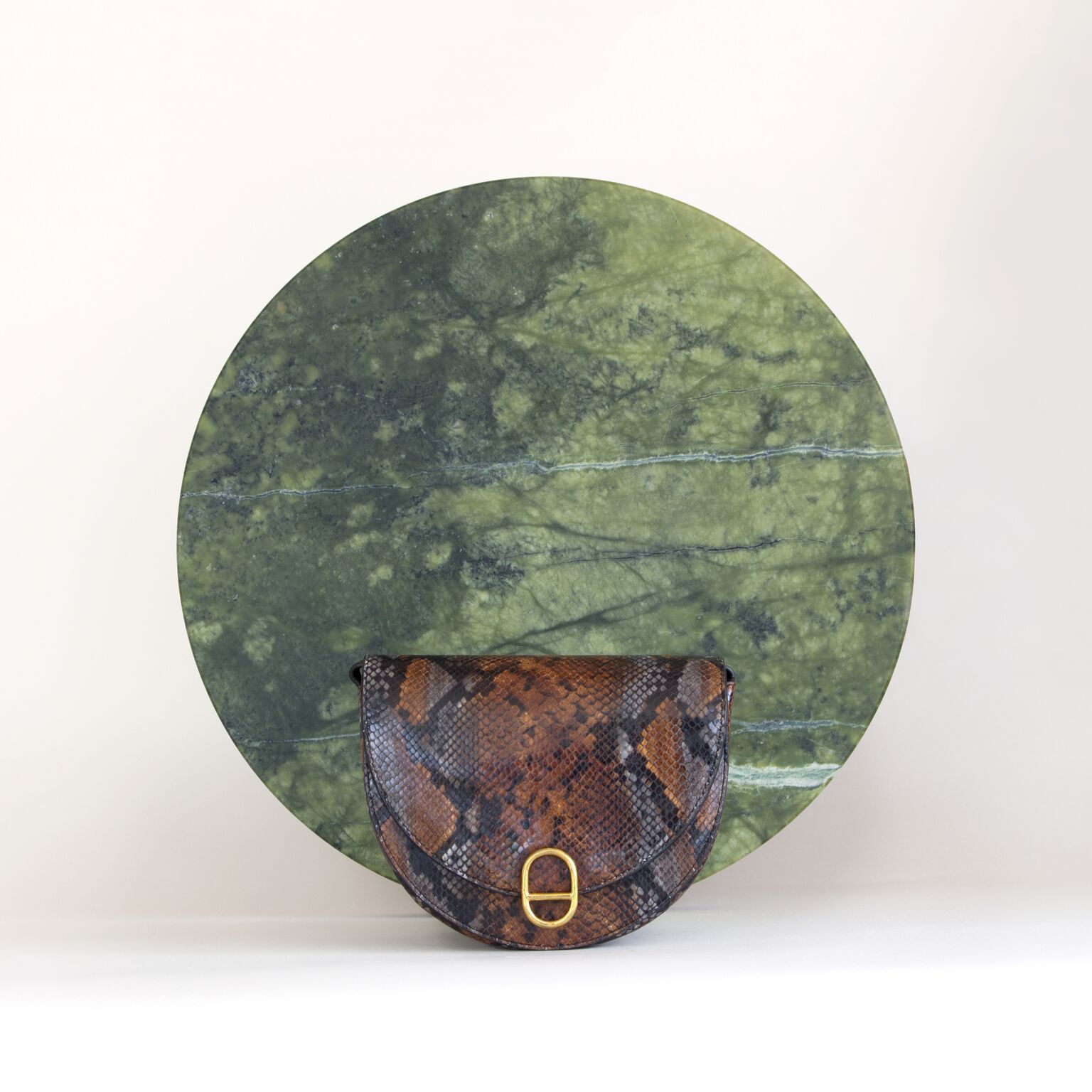 Snake skin patterned purse against circular green stone and white wall