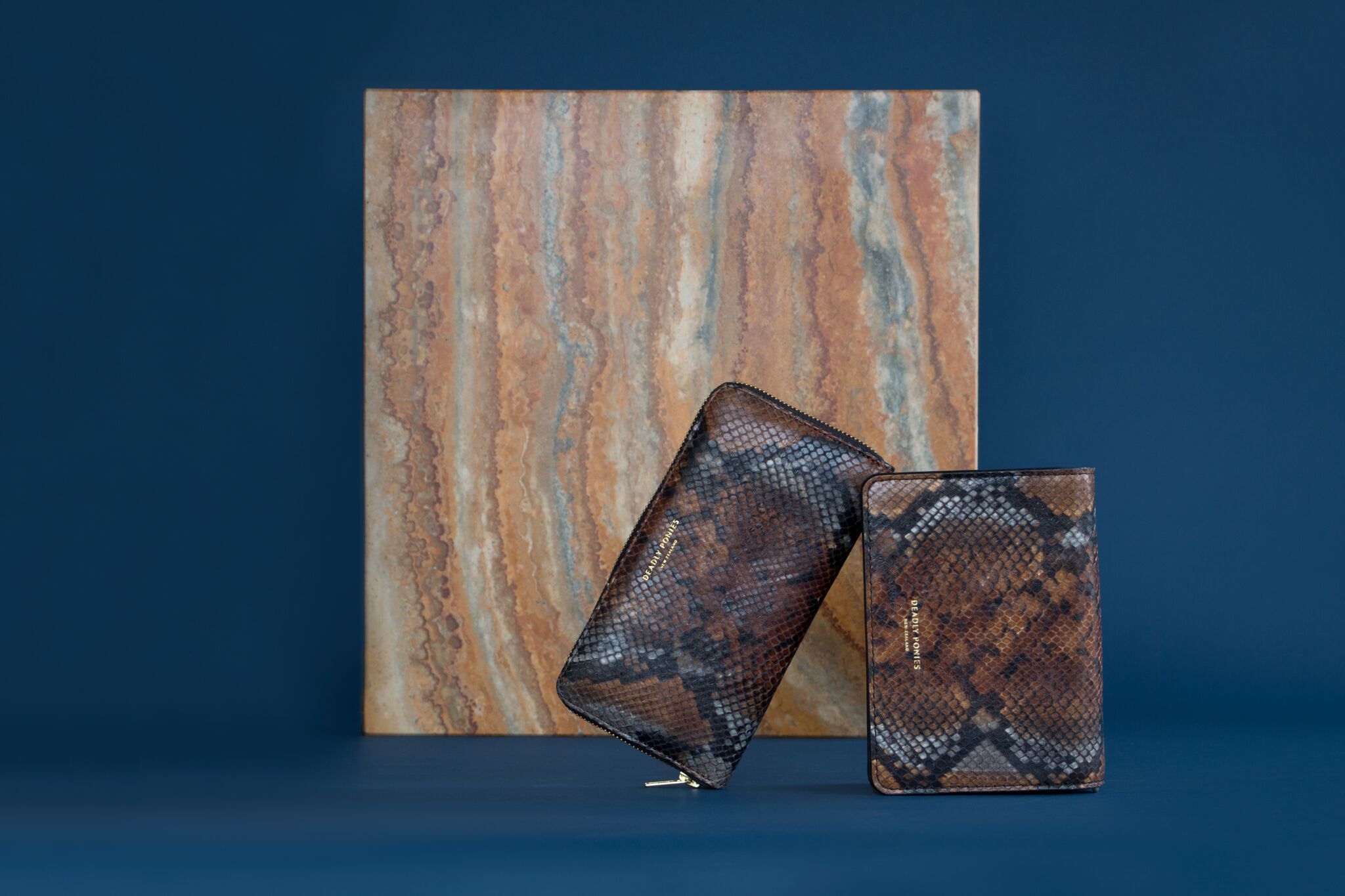 A couple of snake skin patterned wallets against a wooden block and blue background