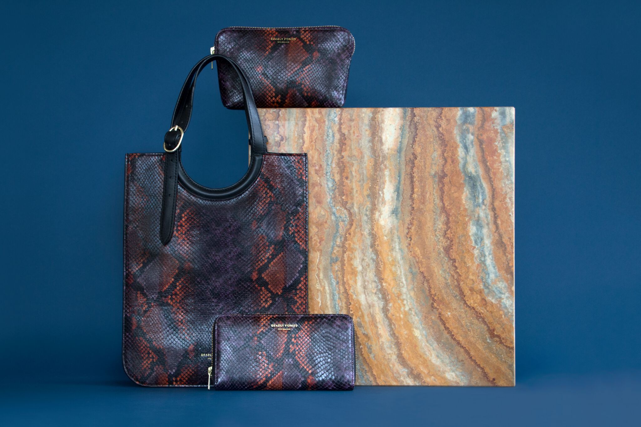 A group of leather red and black bags arranged against a wooden block and blue background