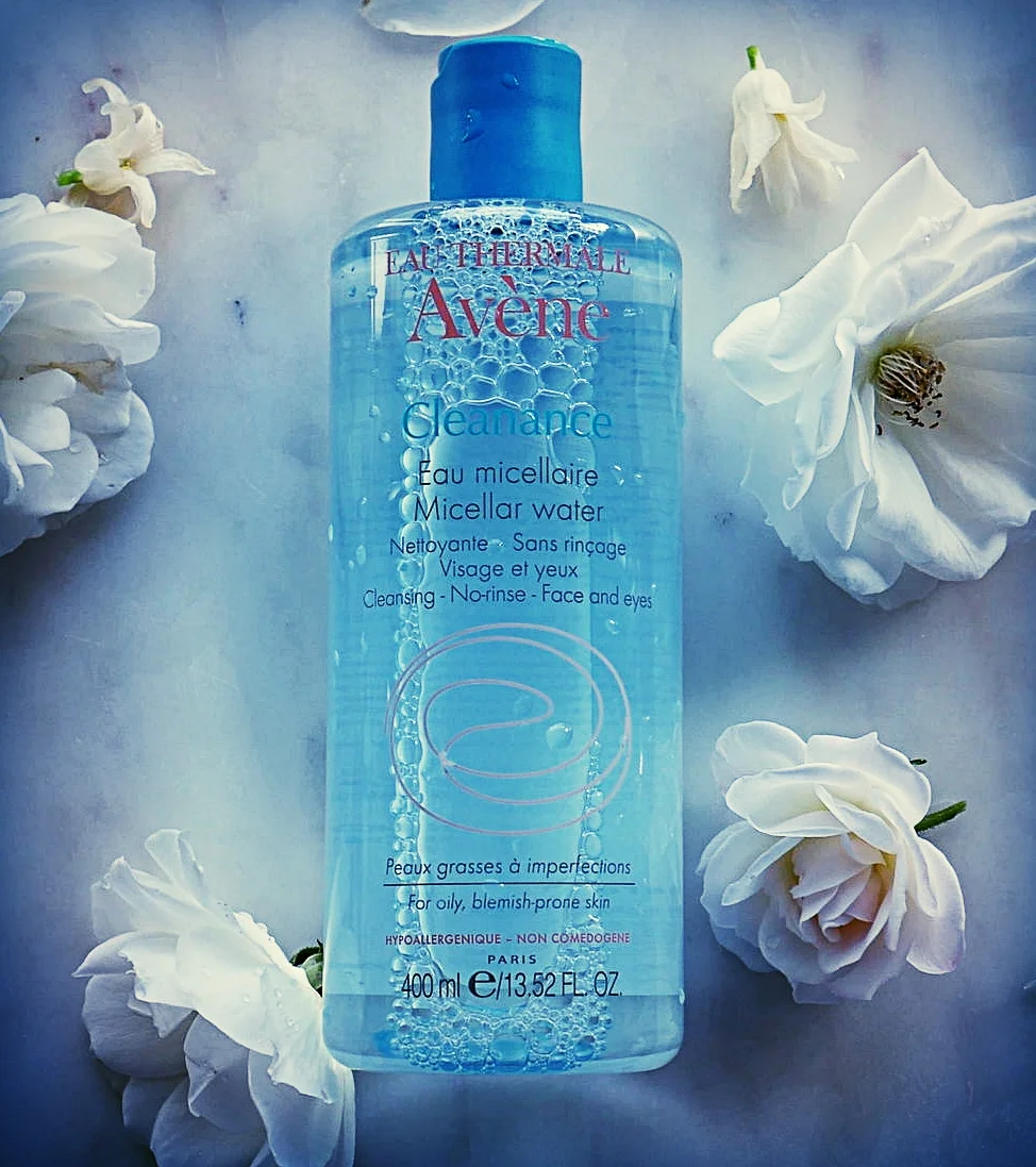 Eau therme avene cleance miceller water in blue bottle laid out on a blue background surrounded by white flowers 