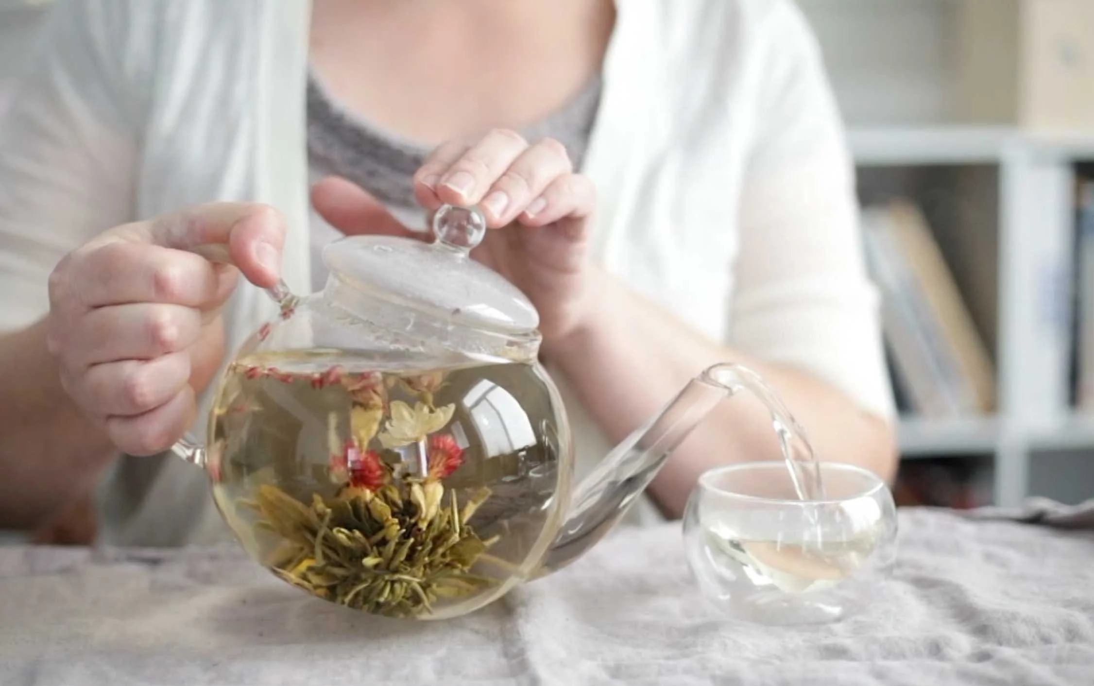 In image of Jaime's hands pouring a clear teapot with a flowering tea inside
