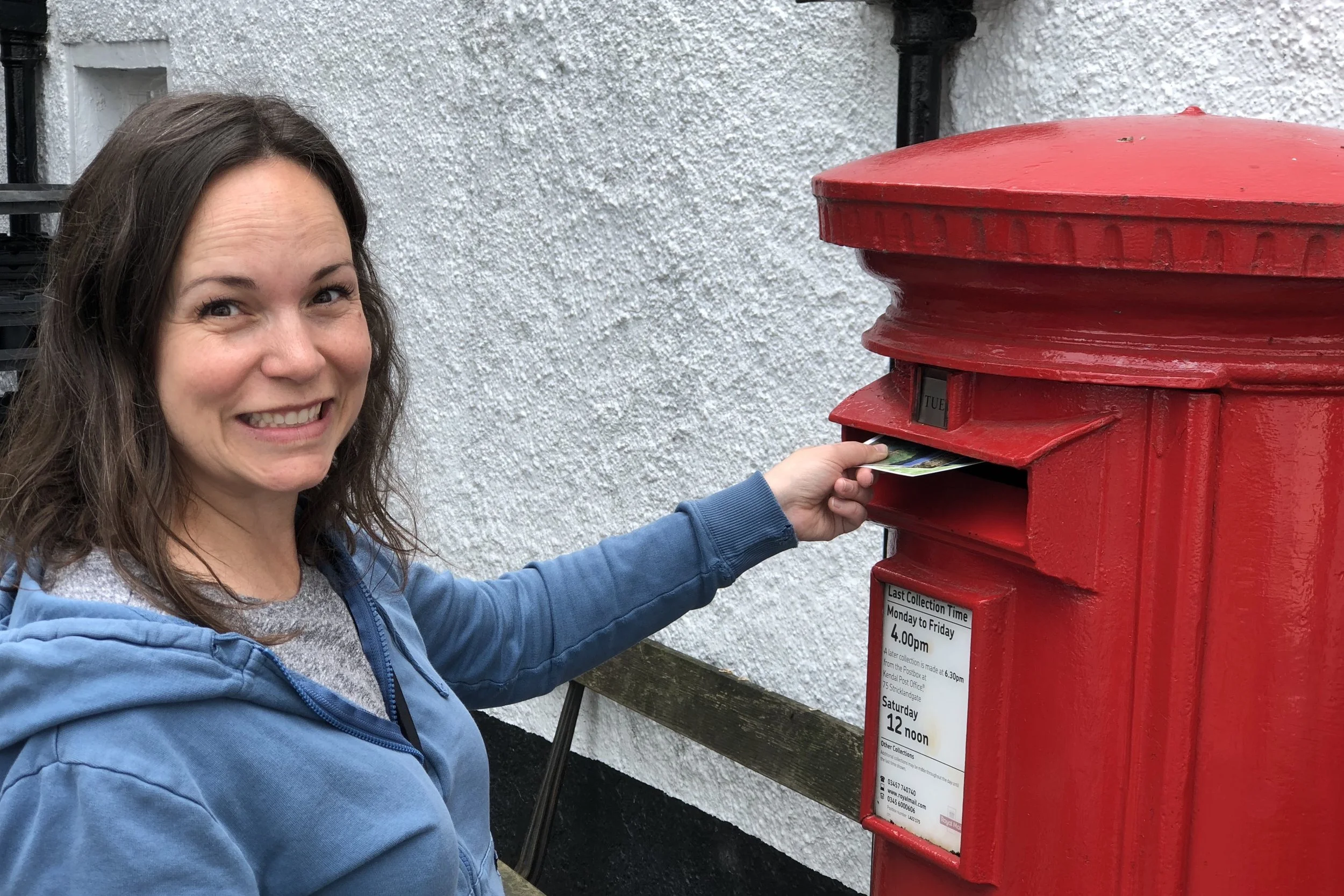 Jaime is grinning while posting mail in a red Royal Mail post box