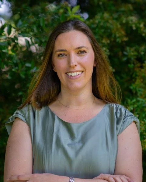 Kate Mattax, ND has a silky blue shirt on and is standing in front of greenery