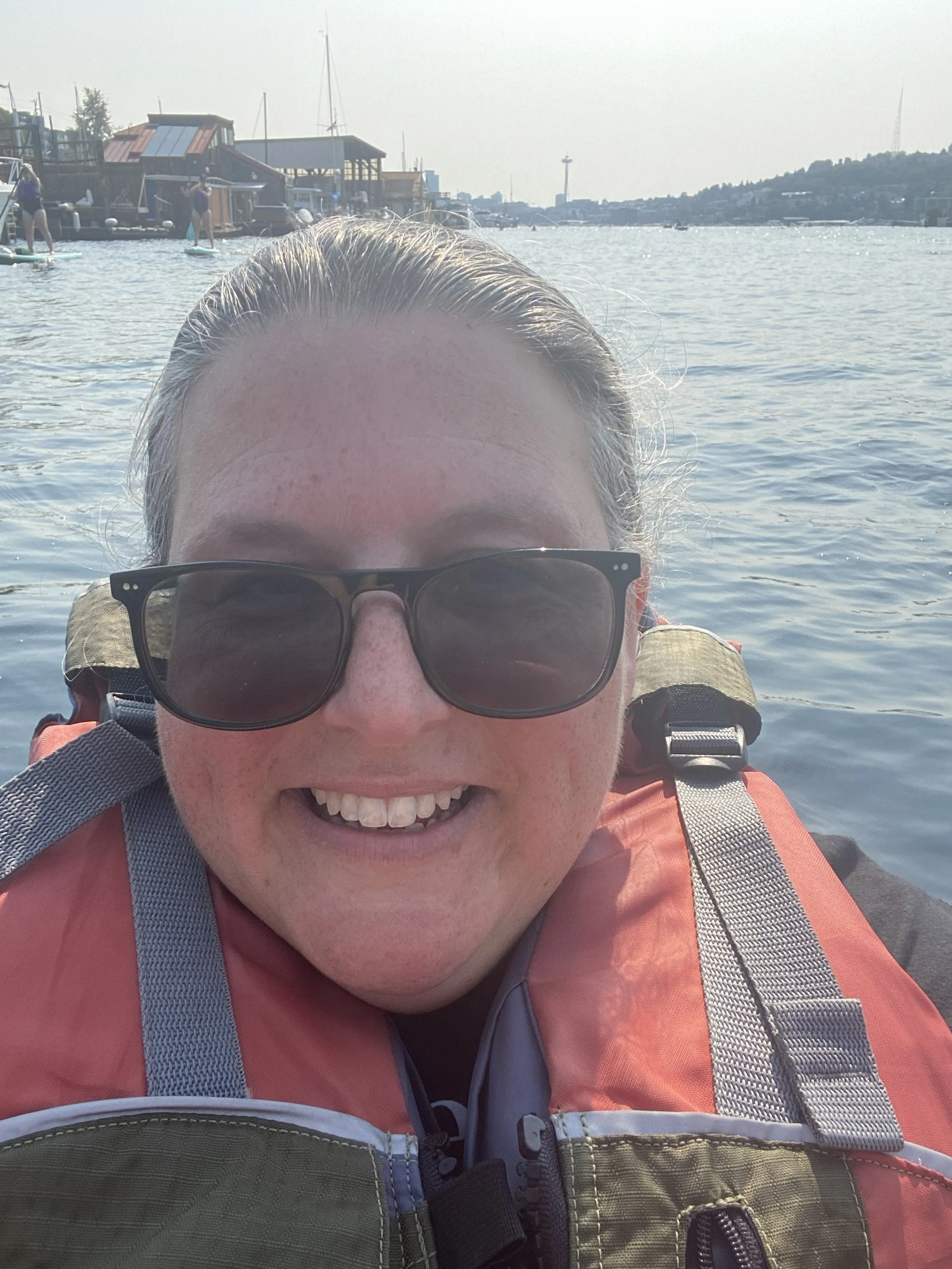 a woman is smiling while kayaking. Wearing an orange life vest