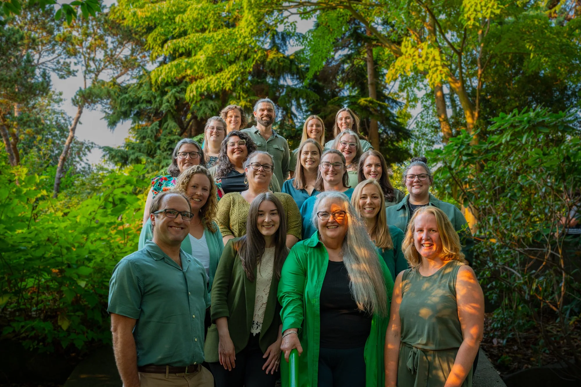 The 19 healthcare providers of One Connection Healthcare are standing on steps surrounded by vibrant green foliage