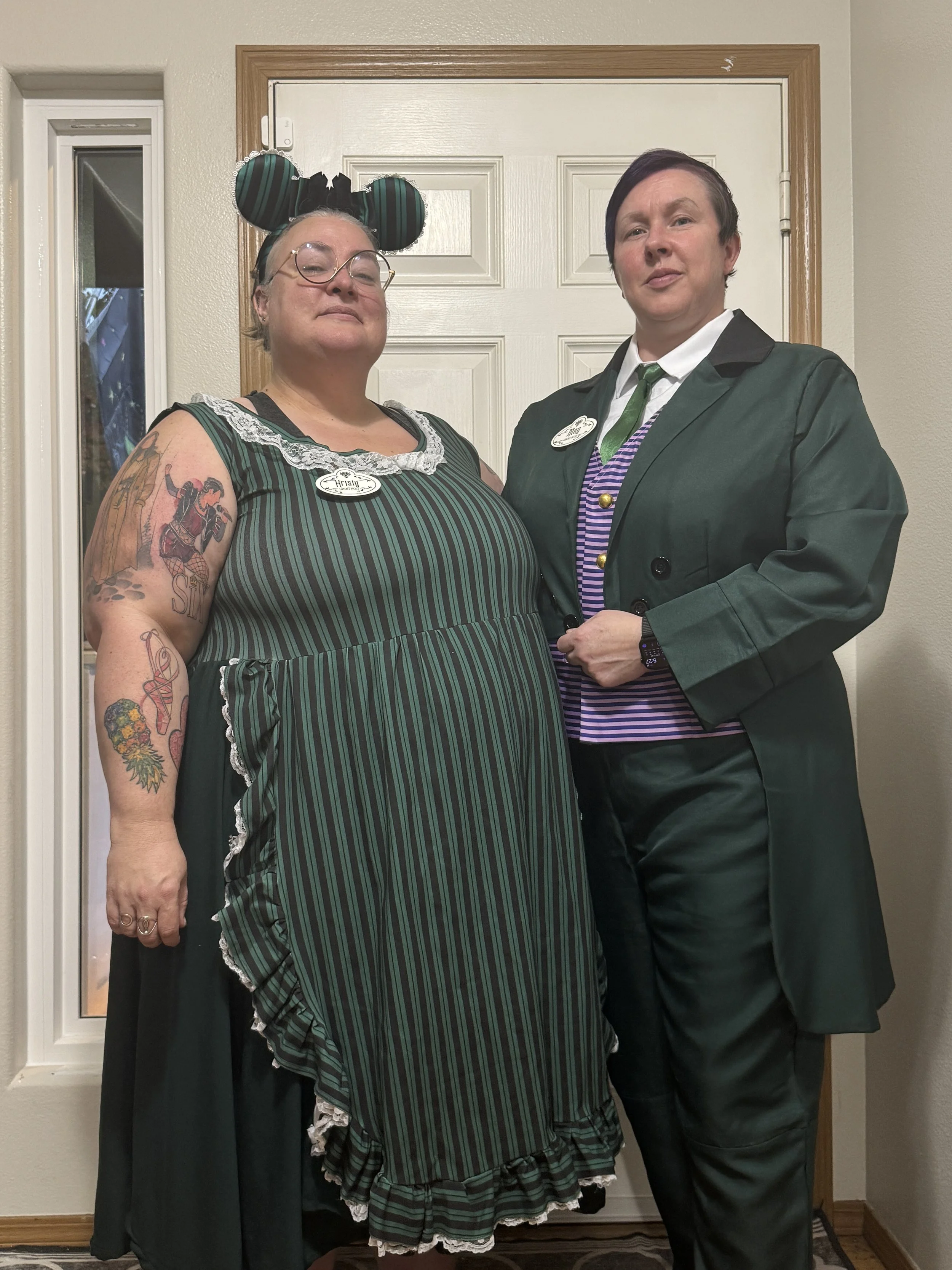 couple dressed in Disney outfit stand in front of door and is smirking